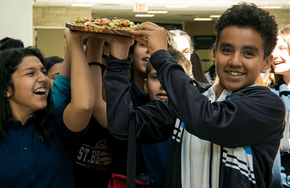 Chartwells K-12 students holding a cutting board with flatbread placed on it