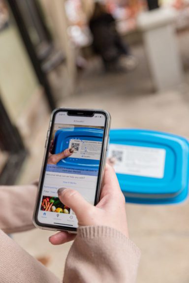 A hand holding a phone and scanning the QR code available on the lid of a Friendlier container 